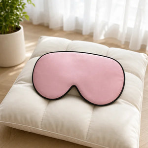 Masque de nuit en soie rose posé sur un coussin dans une chambre lumineuse