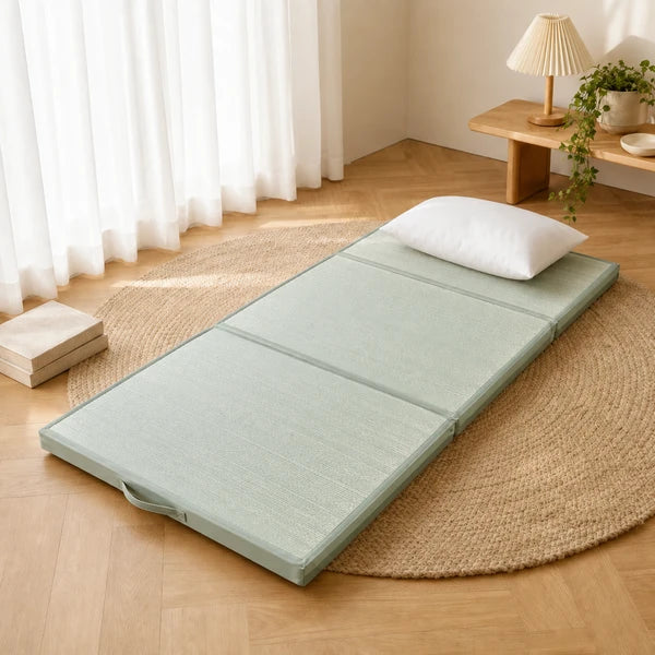 Natte tressee vert clair depliee sur un parquet, oreiller blanc et livres, tapis en jute
