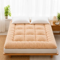 Surmatelas en duvet beige clair posé sur un lit en bois, chambre lumineuse