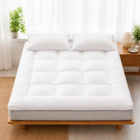 Surmatelas en plume blanc matelassé en carrés posé sur un lit en bois clair, deux oreillers