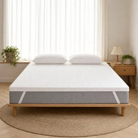 Surmatelas ferme blanc posé sur un lit, bordure grise avec sangles blanches, deux oreillers