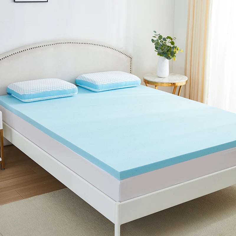 Surmatelas mémoire de forme bleu posé sur un lit à tête de lit capitonnée blanche, deux oreillers bleus