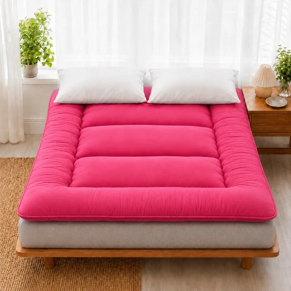 Surmatelas ouate rouge pose sur un lit en bois clair, deux oreillers blancs
