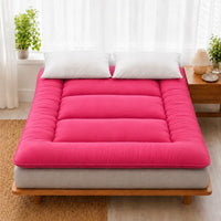 Surmatelas ouate rouge pose sur un lit en bois clair, deux oreillers blancs