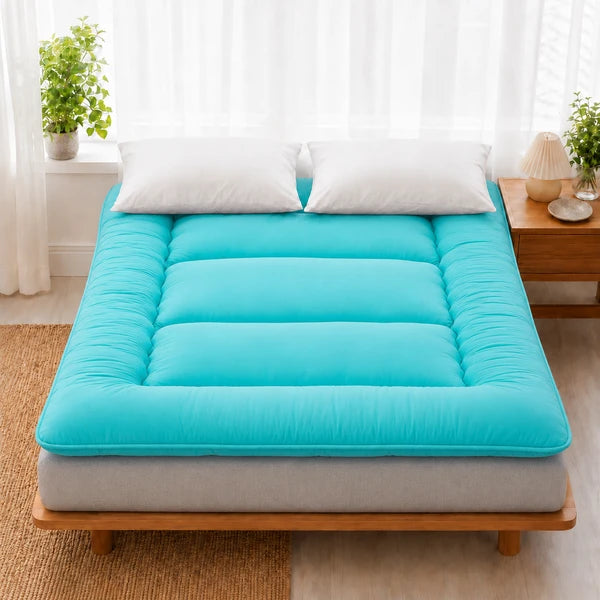 Surmatelas ouate bleu turquoise pose sur un lit en bois clair, deux oreillers blancs
