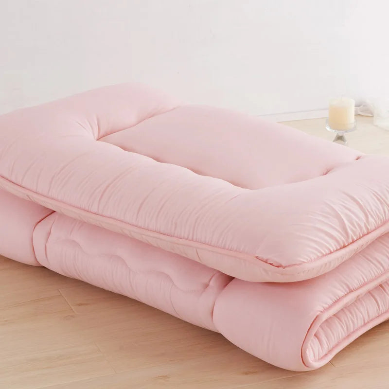 Surmatelas ouate rose plie, pose sur un sol en bois avec une bougie