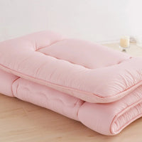 Surmatelas ouate rose plie, pose sur un sol en bois avec une bougie